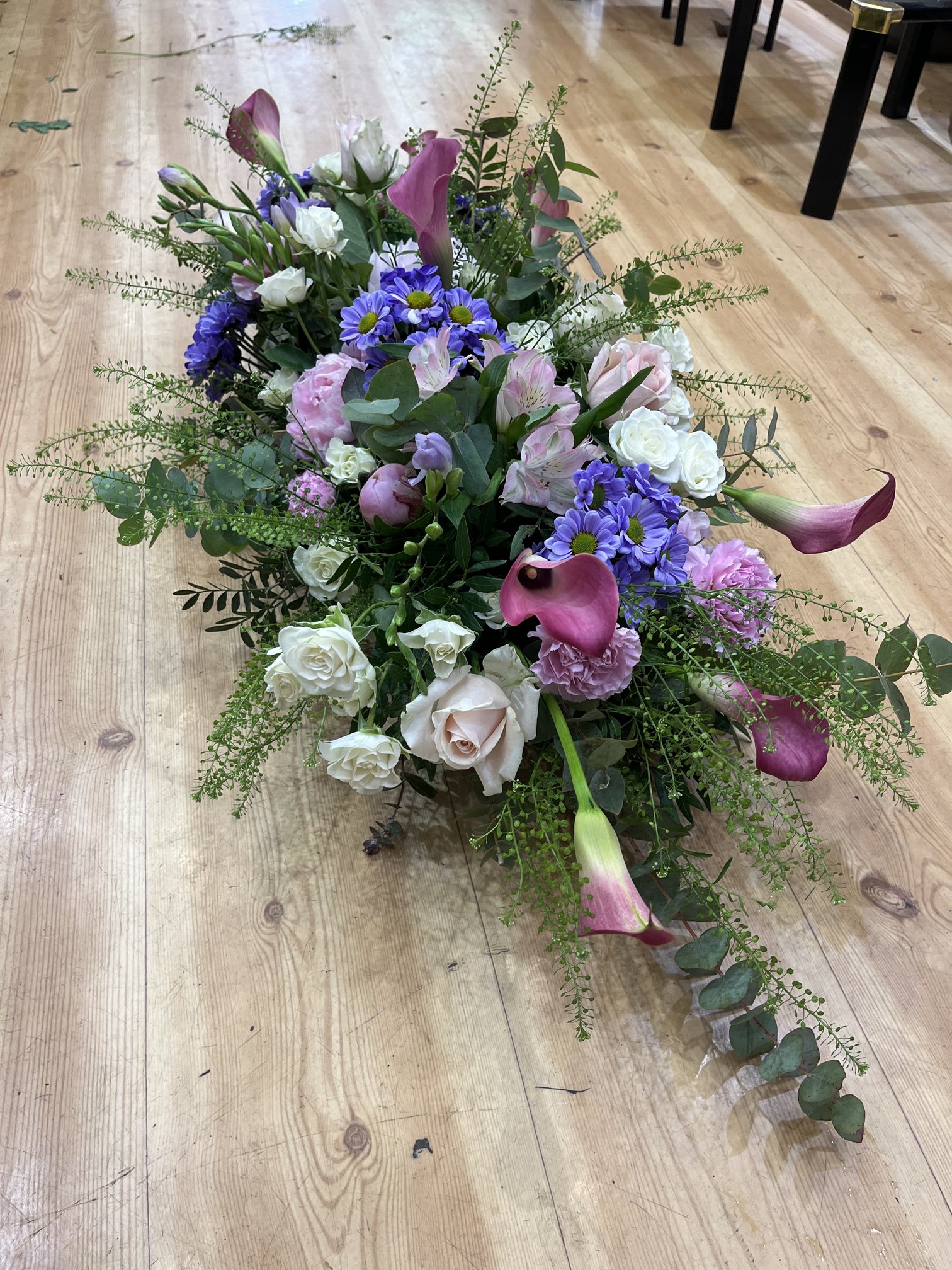 Gerbe de deuil allongée en callas mauves, roses blanches et fleurs bleues