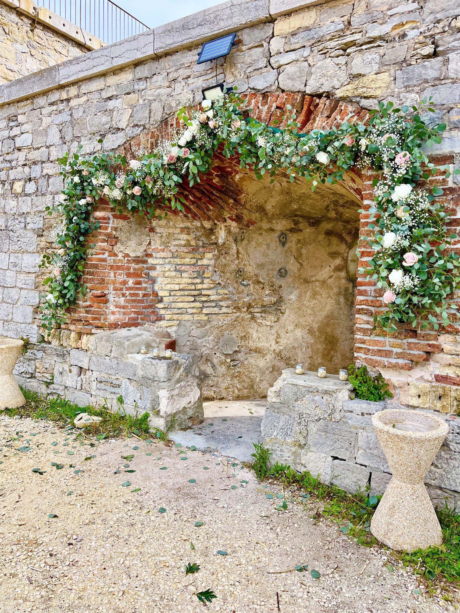 Arche fleurie en roses et eucalyptus sur une arche en pierre pour une cérémonie de mariage
